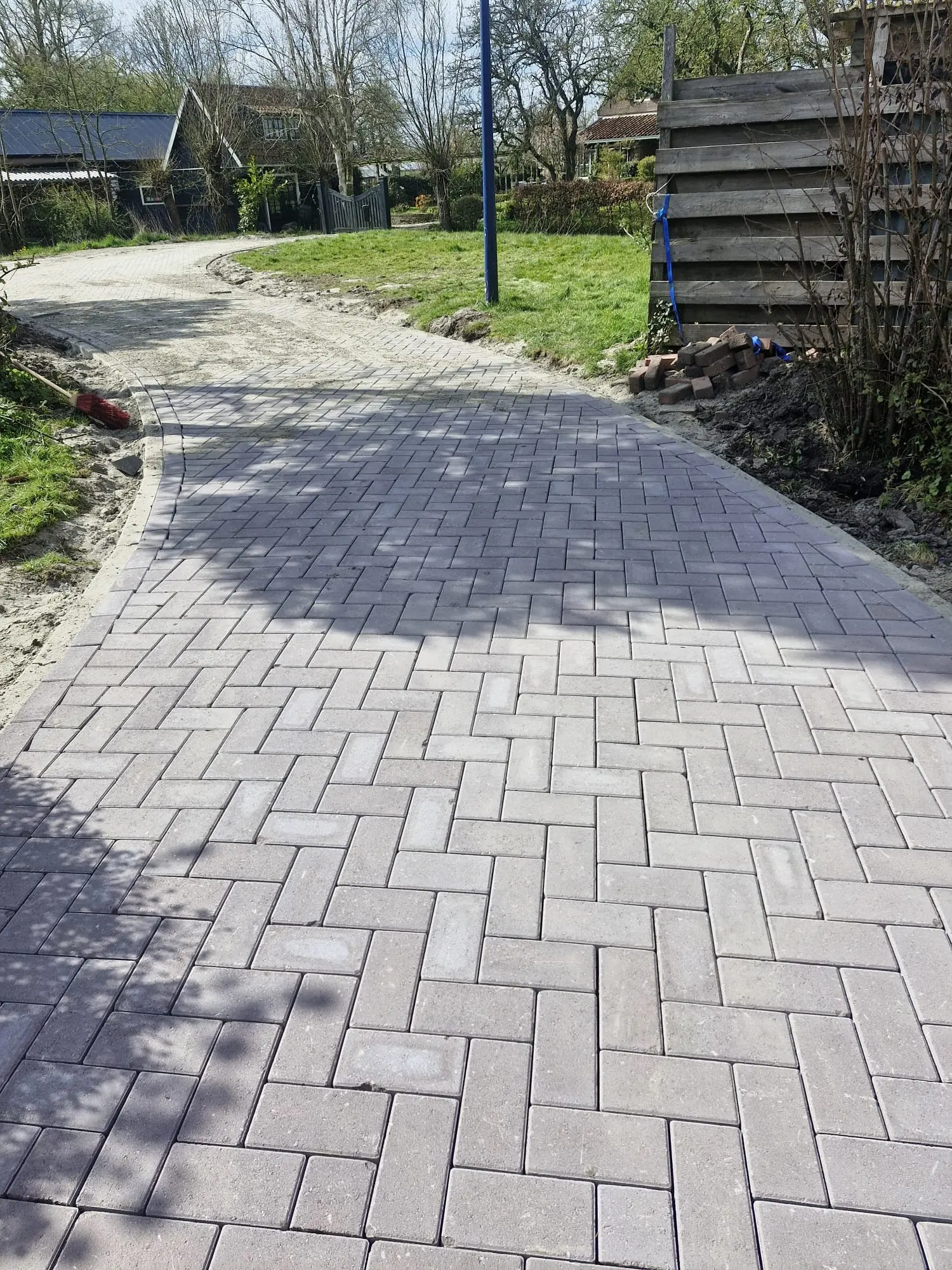 Grijs tuinpad in keperverband dat in een bocht langs het gras loopt