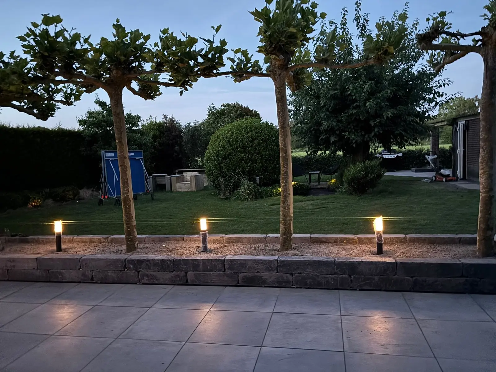Terras met grote donkere tegels en tuinverlichting in de avond