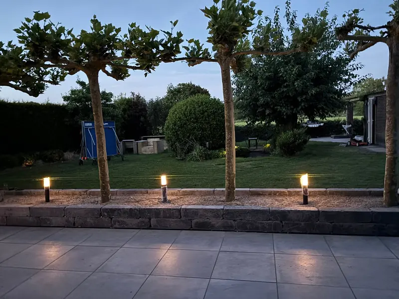 Terras met grote donkere tegels en tuinlampen in de avond