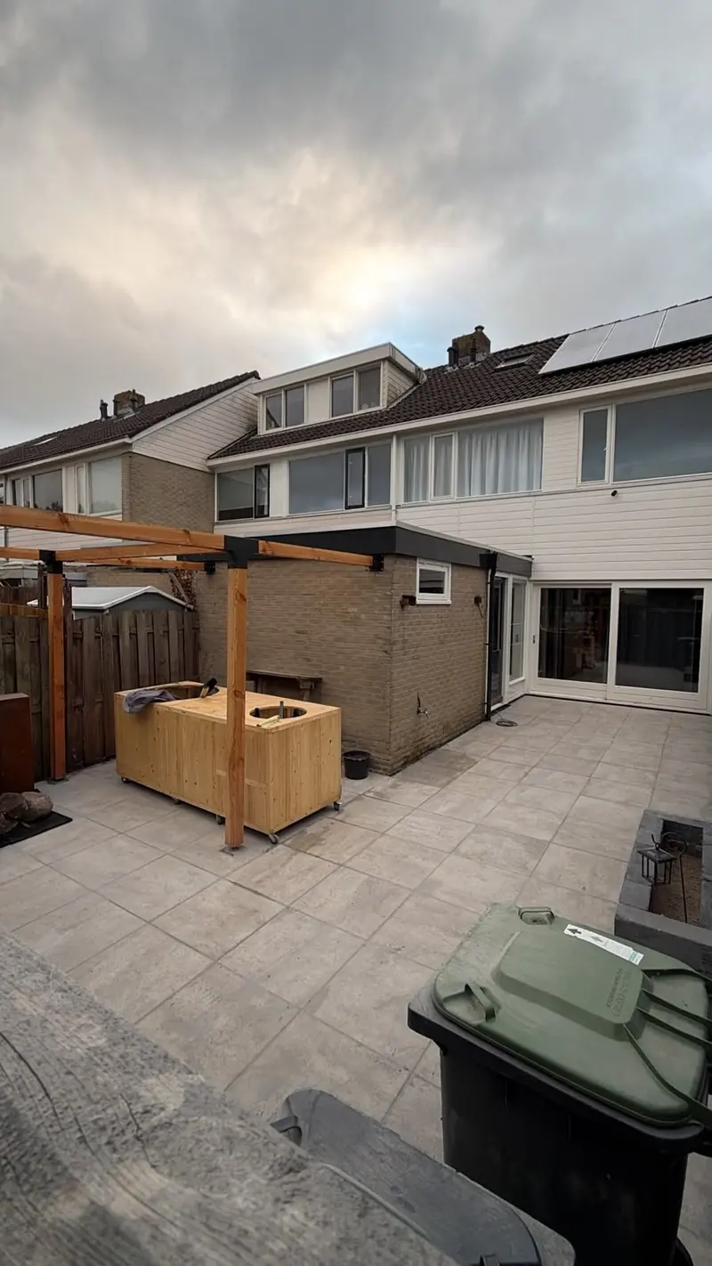 Terras van lichte tegels met een houten pergola en buitenkeuken